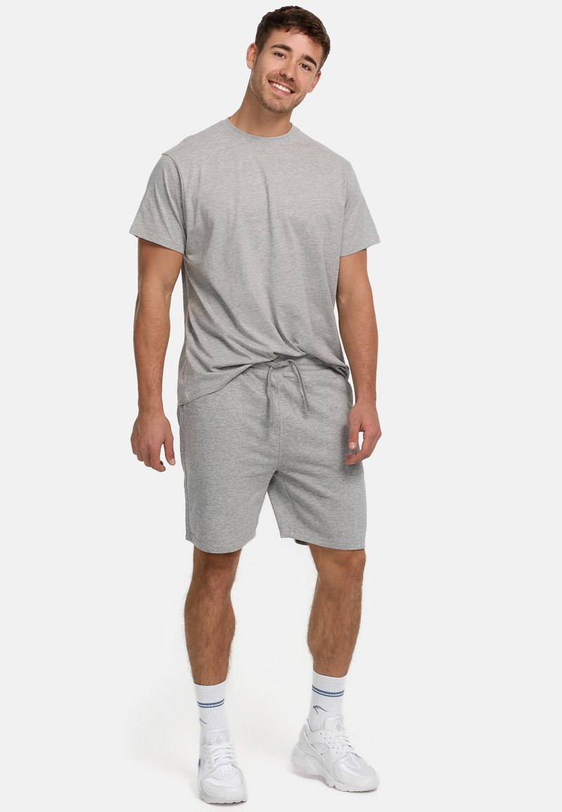 Grå bomulds T-shirt med rund hals og korte ærmer, parret med grå shorts med snøre. Modellen bærer hvide sneakers med blå accenter.
