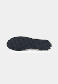 Suola di scarpa con una superficie in gomma nera testurizzata, caratterizzata da un motivo geometrico. Bordo bianco con elementi di design minimi.