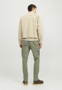Chaqueta de mezclilla beige con un diseño recortado, usada sobre una blusa ligera con estampado, combinada con pantalones cargo verdes y botas marrones.