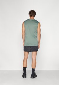 Ærmeløs grøn træningsshirt kombineret med mørke shorts. Designet har en glat tekstur og en afslappet pasform, der er velegnet til motion.