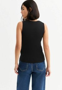 Zwarte mouwloze ribbeltop met een ronde halslijn, een getailleerd ontwerp en een gladde textuur, gecombineerd met hoge taille blauwe denim jeans.