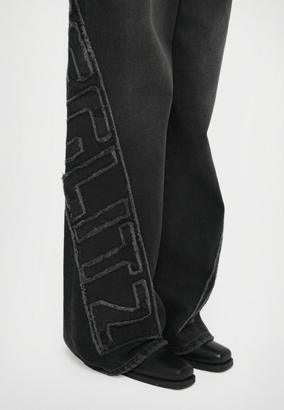 Black denim wide-leg pants with frayed edges, featuring a contrasting textured pattern on the side, paired with black ankle boots.