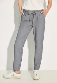 Grå sweatpants med dragsko i midjan, sidofickor, avsmalnande ben och en mjuk textur, tillsammans med vita sneakers med blå detaljer.