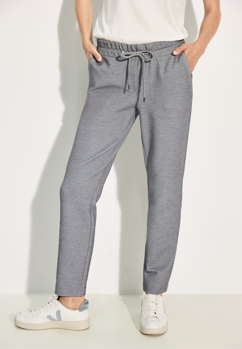 Grå sweatpants med dragsko i midjan, sidofickor, avsmalnande ben och en mjuk textur, tillsammans med vita sneakers med blå detaljer.