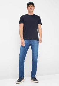 Marineblauwe katoenen t-shirt gecombineerd met blauwe denim jeans. De outfit wordt compleet gemaakt met donkere sneakers en een marineblauwe pet met een lichtblauw accent.