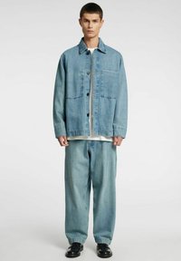 Lichtblauwe spijkerjas met kraag, knopen aan de voorkant en een borstzak, gecombineerd met bijpassende broek met losse pasvorm en zwarte schoenen.