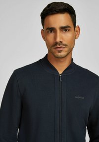 Marineblauer Reißverschlussjacke aus strukturiertem Material, mit hohem Kragen und dezentem HECHTER-Branding auf der linken Brust. Moderne, taillierte Silhouette.