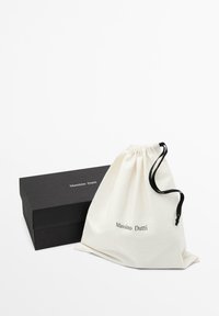 Bílý bavlněný sáček na stažení s černým potiskem "Massimo Dutti" vedle černé obdélníkové krabičky se stejným brandingem.