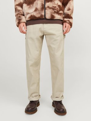 Veste floue marron et beige, pantalon kaki clair avec le bas retroussé, et bottes à lacets marron foncé. Texture douce avec une coupe décontractée.