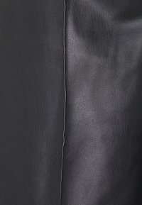 Svart läder med en slät textur och en lätt lyster. Har en synlig söm som löper vertikalt längs kanten.