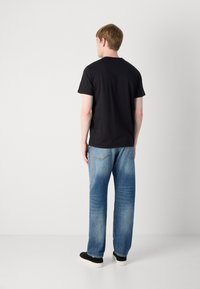 Zwart katoen T-shirt met korte mouwen, gezien vanaf de achterkant, gecombineerd met lichtblauwe spijkerbroek en zwarte schoenen.