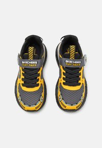 Zapatillas Skechers Tuff Truck en negro y amarillo con parte superior de malla, suela de goma, acentos sintéticos y correa integrada sobre los cordones.