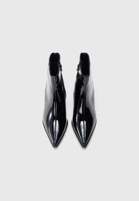 Botas de tornozelo em pele preta envernizada com biqueira pontiaguda, apresentando um fecho de correr lateral e textura suave e brilhante. Linhas limpas e design elegante.