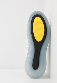 Genomskinlig sula med ett gult strukturerat insats, omgiven av svart gummi och genomskinligt material, med en kurvad och slät design.