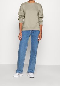 Sudadera holgada verde oliva con puños acanalados, combinada con vaqueros de pierna recta azul claro y zapatillas deportivas blancas. Tela de algodón suave.