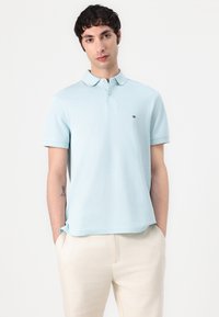 Camisa polo azul claro hecha de algodón suave. Presenta un cuello clásico, mangas cortas y un pequeño logo en el lado izquierdo del pecho.