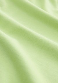 Tissu vert clair avec une surface lisse et légèrement texturée, mettant en valeur des plis et des drapés en coton doux ou un matériau similaire.