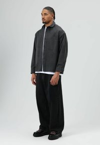 Grijze jas van een wolmix met een kraag, knoopsluiting en lange mouwen, gecombineerd met loszittende zwarte denim broek en zwarte schoenen.