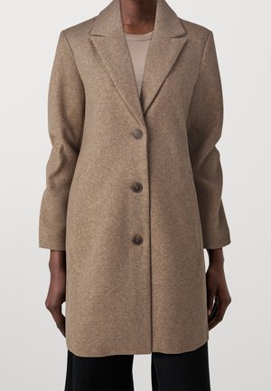 Manteau en laine marron longueur genoux avec trois boutons, porté sur un top côtelé beige et un pantalon noir.
