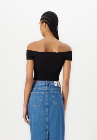 Top nero cropped senza spalline con texture arricciata, abbinato a una gonna di jeans blu a vita alta con uno spacco posteriore e tasche applicate.