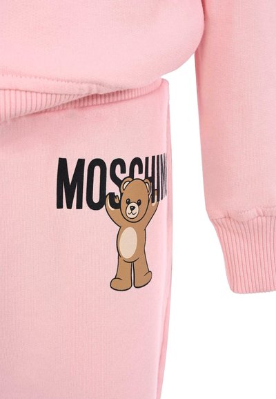 Różowa bluza z ribbowymi mankietami, z ilustracją niedźwiedzia i napisem "MOSCHINO" w czerni. Gładka tekstura, casualowy fason.