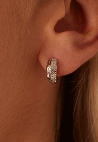 Boucle d'oreille en argent en forme de créole, ornée d'une rangée de cristaux transparents sur le devant, au design courbé lisse et à la texture polie, portée sur une oreille.