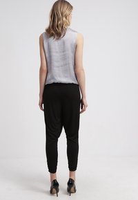 Beżowa bluzka bez rękawów o luźnym kroju w połączeniu z czarnymi zwężanymi spodniami. Czarne buty na wysokim obcasie dopełniają strój.