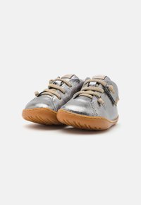 Scarpe in pelle argentata con una finitura liscia, accenti grigi, lacci beige e una suola in gomma marrone flessibile progettata per il comfort e la facilità di movimento.