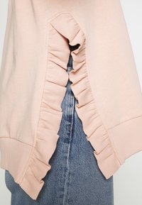 Lichtroze sweatshirt met gerimpelde accenten langs de zijnaad, voorzien van ribbelstructuur en een relaxte pasvorm, gecombineerd met denim.