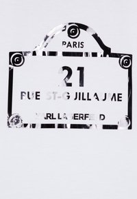 Svartvit grafik som skildrar ett gatustecken med "21 RUE ST-GUILLAUME", omgiven av dekorativa element, märkt med "PARIS" och "KARL LAGERFELD."