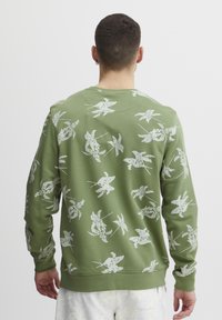 Groene sweatshirt met wit bloemenpatroon, lange mouwen, ronde hals en ribgebreide zoom. De stof lijkt zacht met een licht gestructureerde afwerking.