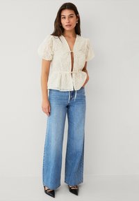Hvid blonde peplum top med puffærmer og tieslutning, parret med lyseblå vidde jeans og sorte spidse hæle.