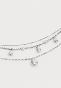 Colier stratificat argintiu, cu mai multe lanțuri și accente de picături strălucitoare, împreună cu un detaliu circular de cristal. Linkurile texturate adaugă un plus de stil designului.