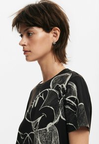 Camiseta negra con un diseño gráfico en estilo tiza en blanco. La camiseta tiene un cuello redondo y mangas cortas, con una textura suave.