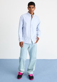 Vaaleansininen raidallinen nappipaita, rento malli, yhdistettynä vaaleisiin farkkuihin ja mustiin lenkkareihin, joissa on vaaleanpunaiset lenkit. Yksinkertainen muotoilu, rento tyyli.