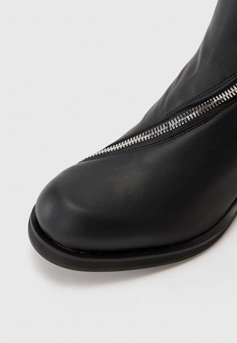 Schwarze Leder-Ankle-Boots mit einer runden Zehenpartie, versehen mit einem metallischen Reißverschlussakzent an der Seite und einer matten Oberfläche am Schaft.