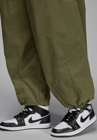 Vihreät, löysät housut, joissa on joustavat hihnat, yhdistetty korkeakorkoisiin mustiin ja valkoisiin Nike-tennareihin, joilla on logo sivussa.