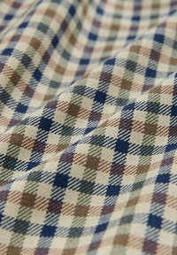 Baumwollstoff mit einem mehrfarbigen Karo-Muster in Marineblau, Grün und erdigen Tönen auf einem beigen Hintergrund. Die Struktur des Gewebes ist sichtbar.