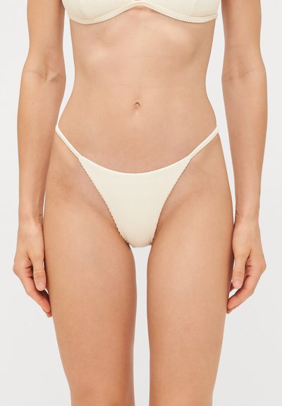 Bas de bikini beige côtelé avec fines bretelles latérales, présentant une coupe haute des jambes et une texture subtile pour plus de détails visuels.