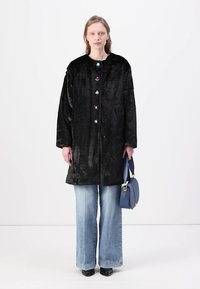 Črn umetni krzneni plašč z zaobljenim ovratnikom, okrašen z barvitimi cvetličnimi gumbi, oblečen nad svetlo modrimi širokimi jeans hlačami, v kompletu z modro torbico.