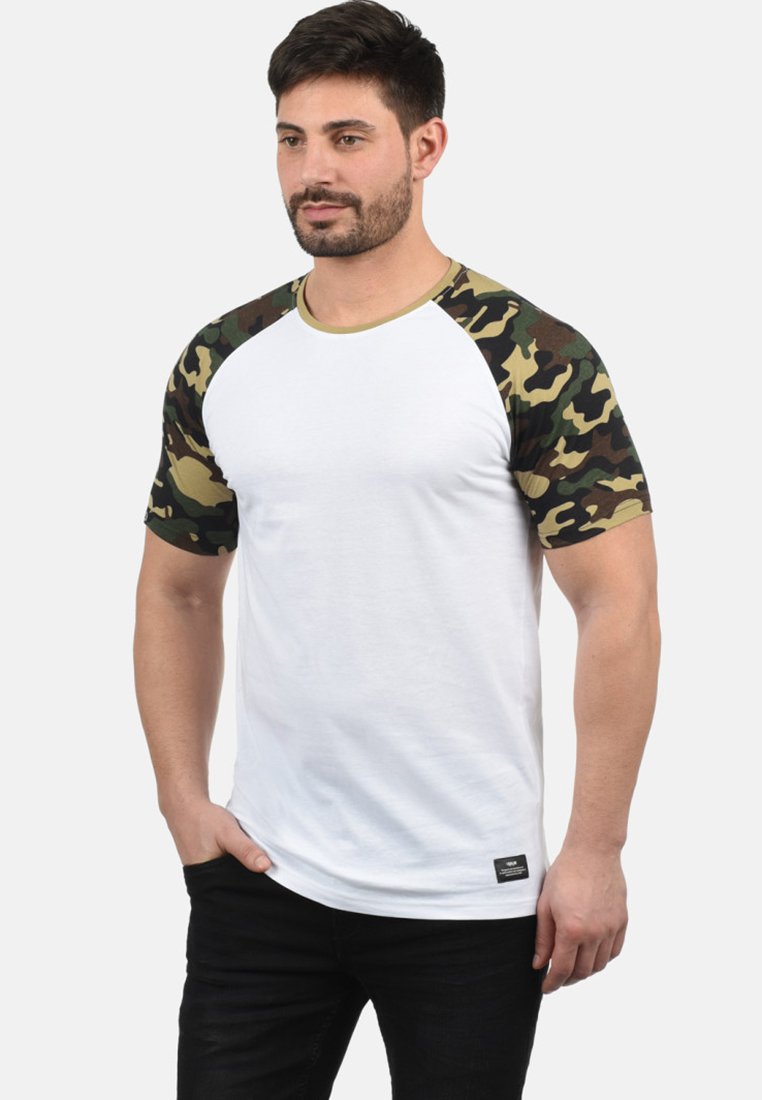 T-shirt bianco a maniche corte con scollo rotondo e maniche a motivo camouflage. Presenta un'etichetta del marchio nera sul fondo.