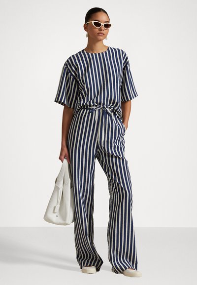 Navy and cream striped two-piece outfit featuring a loose short-sleeve top and wide-leg pants, paired with white accessories and sunglasses.