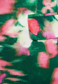 Tessuto verde con un motivo floreale sfocato in tonalità di rosa e rosso. Una tasca è visibile nella parte superiore, rifinita in verde.