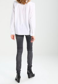 Chemise blanche à manches longues avec une texture subtile, associée à un jean gris cintré et des bottines noires à talons. Silhouette simple et moderne.