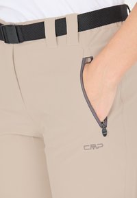 Beige lette bukser med en lynlås lomme, sort bælte og grå detaljer. Har en glat tekstur og diskret branding.