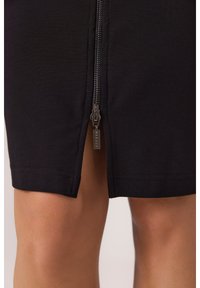 Czarna spódnica ołówkowa z przednim zamkiem błyskawicznym i metalowym uchwytem oraz rozcięciem do połowy uda. Wykonana z teksturowanej, elastycznej tkaniny.