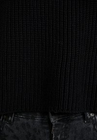 Svart stickad tröja med ribbad textur, parat med mörka, mönstrade svarta jeans med en slät och elegant yta.