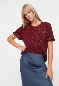 Burgundské top s flitry a krátkými rukávy, kulatým výstřihem, doplněný saténovou sukní navy. Top má texturovaný, lesklý povrch.