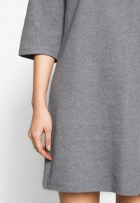 Vestito grigio a maglia con maniche corte, caratterizzato da una vestibilità comoda e una fessura laterale. Tessuto ricco e design semplice per comfort e versatilità.