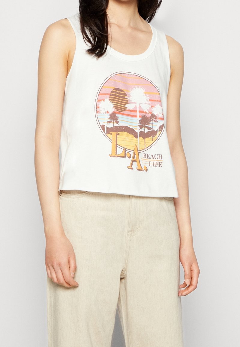 Crop top bianco senza maniche con una grafica circolare che rappresenta un tramonto, palme e il testo "L.A. BEACH LIFE" in toni di marrone e arancione.